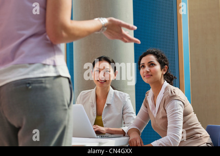 Office workers using laptop and looking at colleague Stock Photo