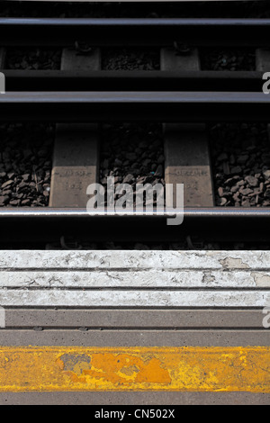 Yellow and white paint on platform of London train station and tracks and stones in background Stock Photo