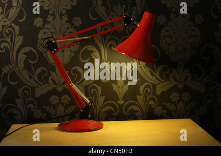 A red desk lamp on a table in front of black and silver wallpaper Stock Photo