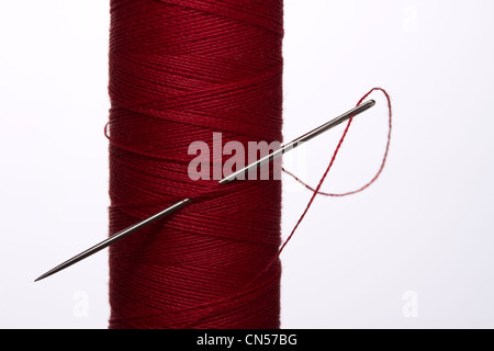 Needle stuck in the side of a reel of red cotton Stock Photo