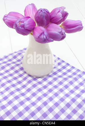 Violet Tulips in Vase on Violet Gingham Tablecloth on White Wooden Table Stock Photo