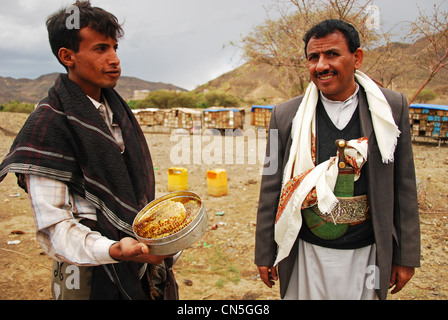 Yemen, Inland, traditional dressed man looking honeycomb seller with beehives locker in the background Stock Photo