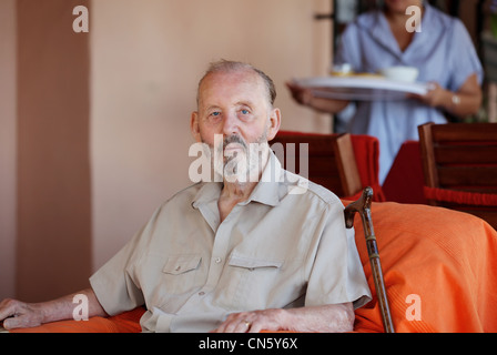 elderly senior man with home help or carer in residential home bringing meal Stock Photo