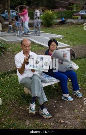 A couple read newspapers while people working out near Samila Beach, Songkhla, Thailand Stock Photo