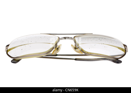 Folded old, dirty eyeglasses with thick bifocal lens in gold metal frame. Glasses of elderly man. Speckled dirt on lens. Stock Photo