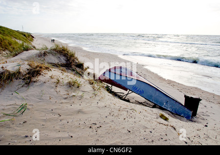 old rusty boat with number lie on sea sand dunes beach overwinter. people walking by seaside. Stock Photo