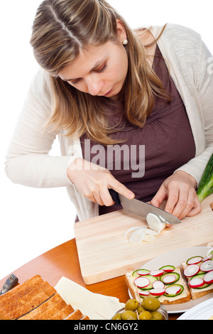 Young beautiful woman chopping fresh spring onion and preparing sandwiches, isolated on white background. Stock Photo