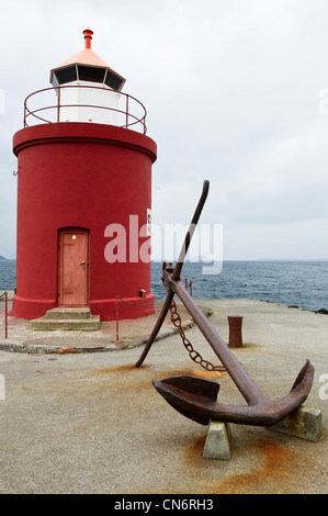A rusty ships anchor with a red and white lighthouse looking out on to a fjord Stock Photo