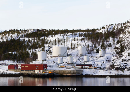 An oil storage facility on the shores of a fjord with a snow covered mountain behind taken in landscape format Stock Photo