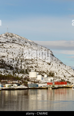 An oil storage facility on the shores of a fjord with a snow covered mountain behind taken in portrait format Stock Photo
