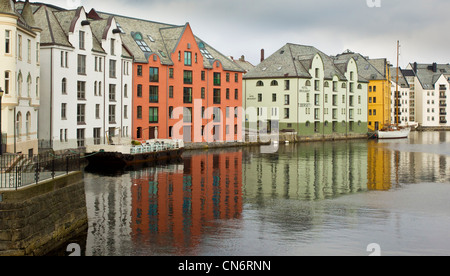 An old barge and a yacht moored up on the side of a river next to several coloured buildings Stock Photo