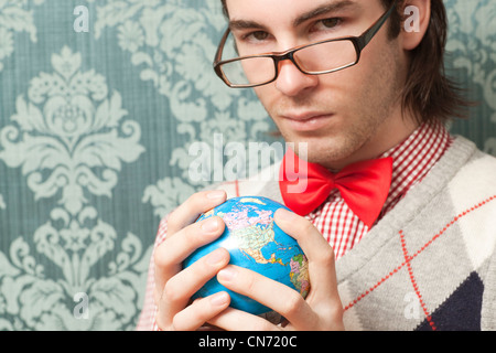 Portrait of young caucasian man wearing glasses holding a globe in both hands looking at camera. Stock Photo