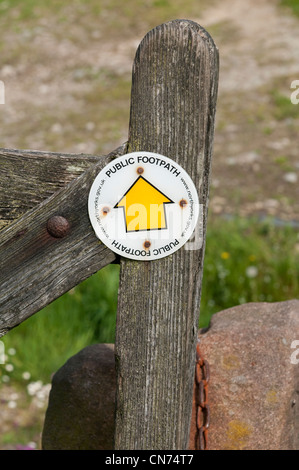 Close-up of circular yellow waymarker public footpath sign with yellow arrow symbol, on wooden gate (right of way) - North Yorkshire, England, UK. Stock Photo