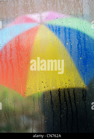 Raindrops on a window pane with a person holding a rainbow coloured umbrella outside