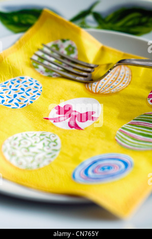 A yellow serviette decorated with an Easter design resting on a dinner plate Stock Photo