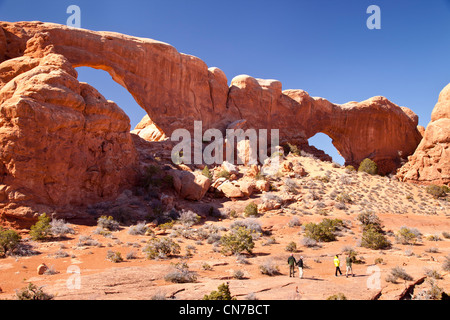 Tourists walk below the massive double arches of the North and South Windows, Arches National Park, Utah USA Stock Photo