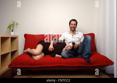 Happy young couple sitting together on a red sofa in the living room Stock Photo