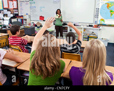 interracial inter multi ethnic racial diversity racially diverse multicultural cultural Students raise raising hands Teacher facing away front Stock Photo