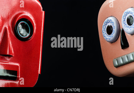 Close up of the faces of two metal, wind-up robots on a black background. Stock Photo