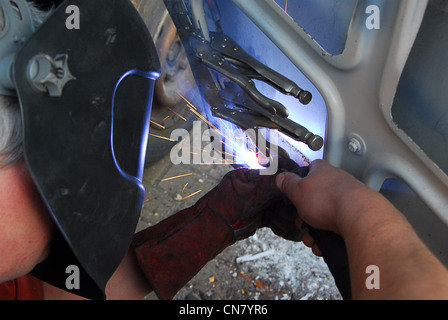Welder repairing camper door during a motor-home restoration project wearing a welding helmet & sparks flying Stock Photo