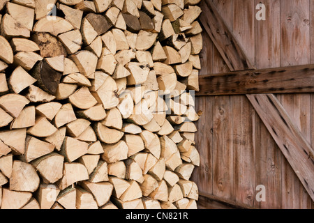 Piles of sawn logs and open door, ready for a winter home fire, stays dry under cover on a small holding. Stock Photo