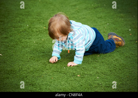 Cute little child girl crawling on the green grass in the park, summer Stock Photo