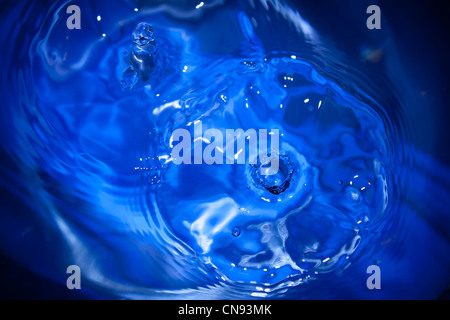Water dripping into vivid blue water creating ripples Stock Photo