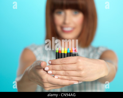 beautiful young woman, holding a few color crayons, smiling, on blue background Stock Photo