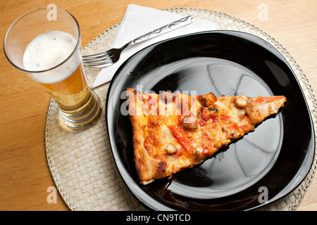 A single slice of buffalo chicken pizza and a glass of golden lager beer. The perfect weekend take out dinner. Stock Photo
