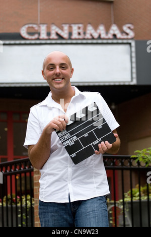 A young man or movie critic holding a movie directors clap board in front of the cinemas. Stock Photo