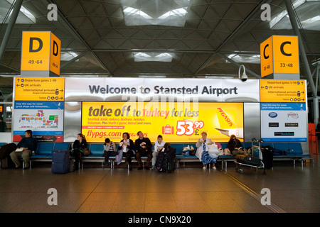 Passengers sitting by the Welcome to Stansted airport signs in the interior of the terminal Stock Photo