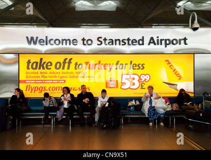 Passengers sitting by the Welcome to Stansted airport signs in the interior of the terminal Stock Photo
