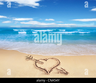 Heart with arrow, as love sign, drawn on the beach shore, with the see and sky in the background. Stock Photo