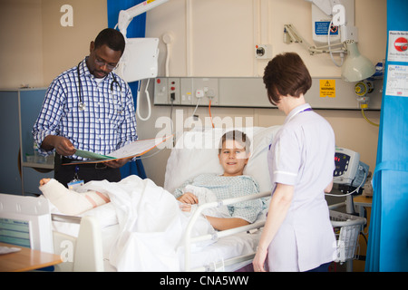 A young boy is checked by a doctor and nurse on a children's hospital ward after an operation UK Stock Photo