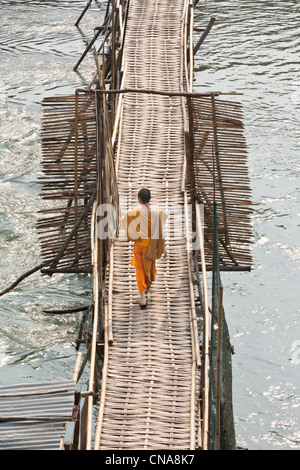 A young Buddhist monk walking across a bamboo bridge in Luang Prabang, Laos
