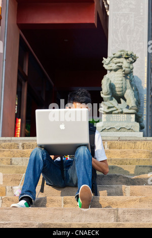 Young man working on Apple MacBook laptop computer seated on the steps of Wenwu Temple, Sun Moon Lake, Taiwan. JMH5881 Stock Photo