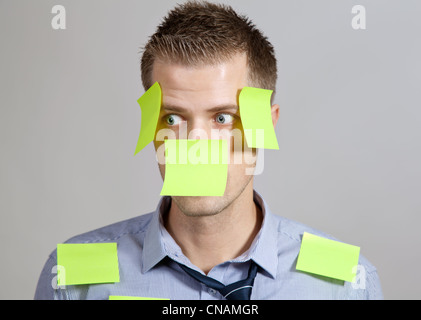 Confused businessman with post it notes on face and clothes Stock Photo