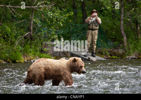 Fisherman in action. He stands in water and holds fly rod in one hand and  spoon in the other one. Also adult has a fishing net on the back. Green  Stock Photo - Alamy