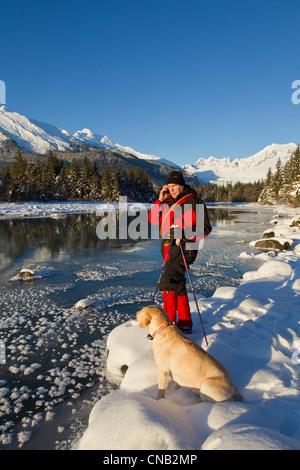 Nordic skier stops to answer his cell phone while his dog sits beside him, Mendenhall River, Juneau, Southeast Alaska, Winter Stock Photo