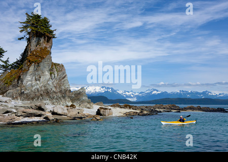 A water level view of a sea kayaker paddling in calm waters along a shoreline near Juneau, Inside Passage, Alaska Stock Photo