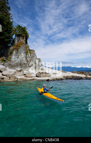 A water level view of a sea kayaker paddling in calm waters along a shoreline near Juneau, Inside Passage, Alaska Stock Photo