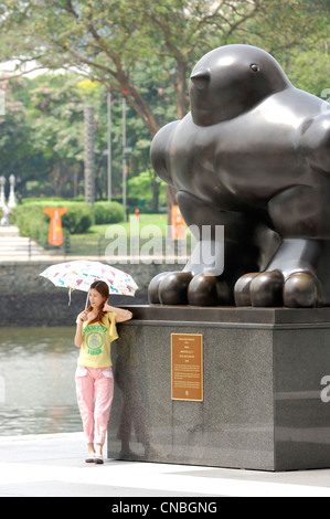 Singapore, business district, young woman with umbrella posing in front of the Bronze sculpture called the bird of the sculptor Stock Photo
