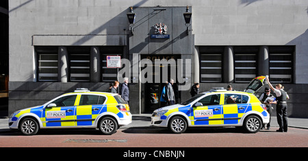 Police officers in uniform beside parked police cars outside City of London Bishopsgate Police station entrance & blue lamps & unconnected passers-by Stock Photo