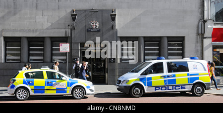 Police officers in uniform beside parked police cars outside City of London Bishopsgate Police station entrance & blue lamps & unconnected passersby Stock Photo