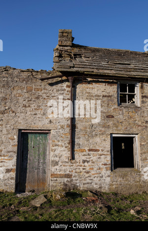 A derelict house and  farm buildings, a textured paint peeling door with rubble surrounding as it gradually falls to ruin Stock Photo