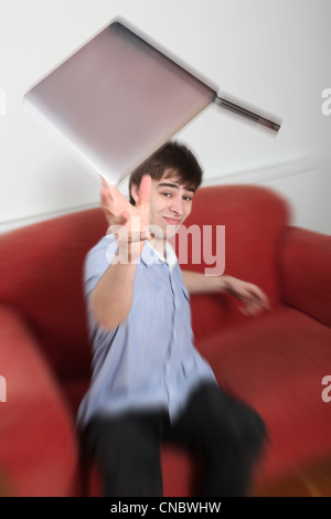 Young man throwing a laptop in frustration Stock Photo