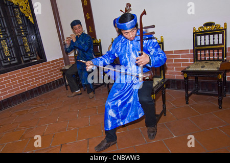 Horizontal close up view of traditional Vietnamese musician playing the dan nhi or vertical violin in bright coloured costume. Stock Photo