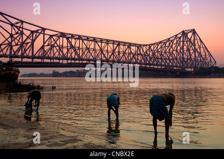 India, West Bengal, Kolkata (calcutta), family cleaning cooking utensils in the Hooghly river with Howrah suspension Bridge Stock Photo