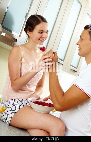 Image of happy woman looking at her husband with spoonful of raspberries Stock Photo