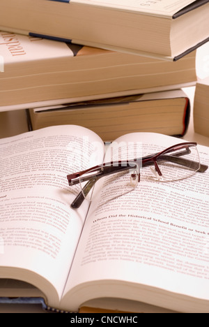 Pile of books with open book and reading glasses. Stock Photo